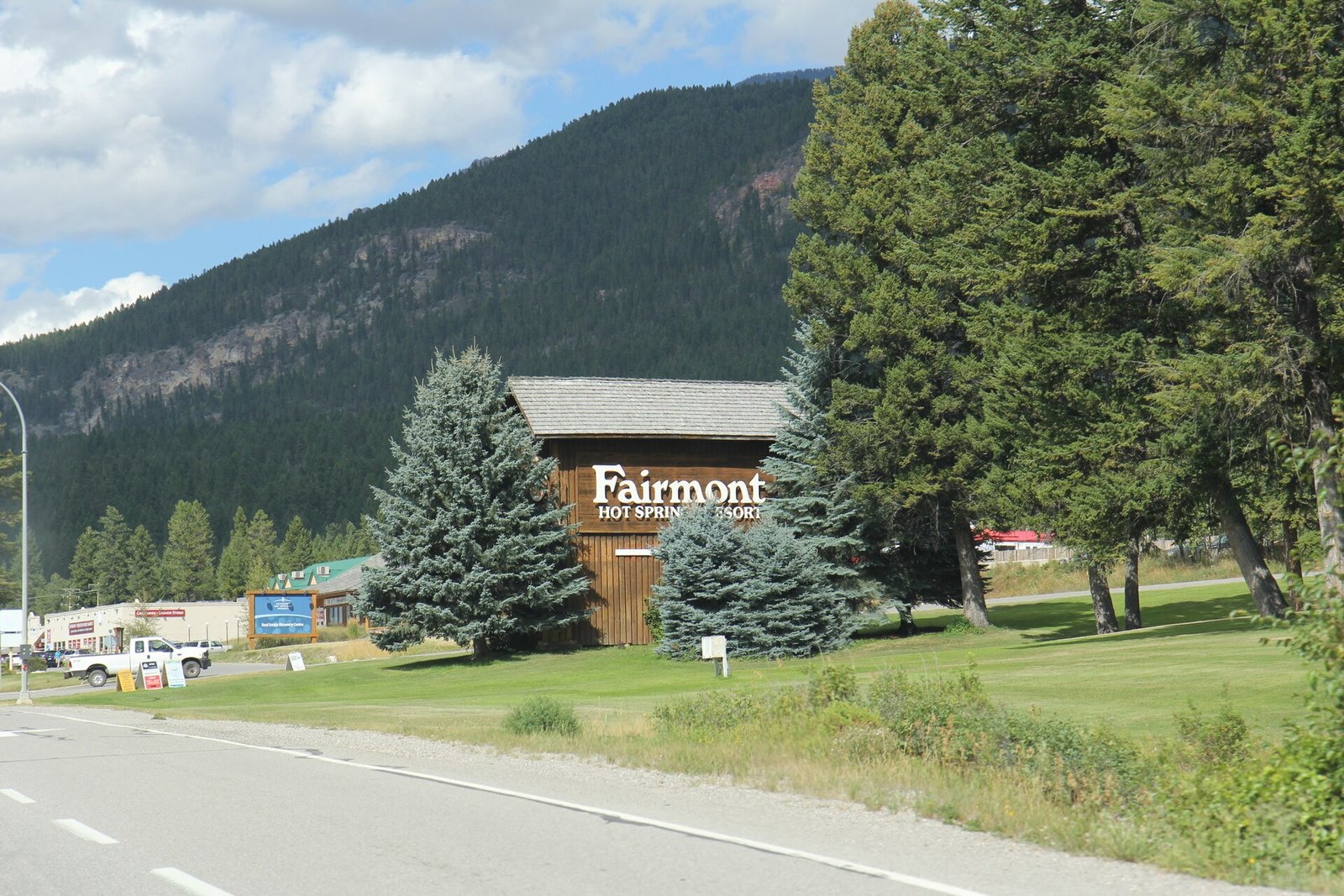 Fairmont Hot Springs Resort sign beside highway below forested mountain