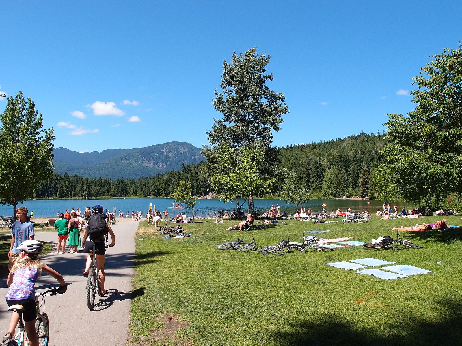 Cyclists on paved path beside busy lakeside park in Whistler
