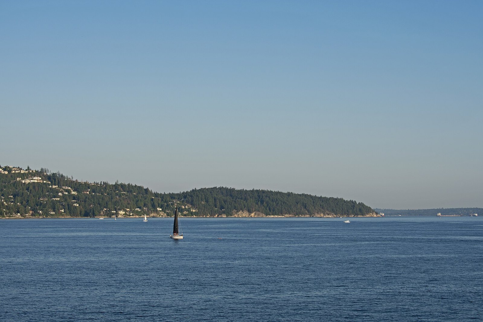 Sailboat off forested West Vancouver shoreline near Point Atkinson